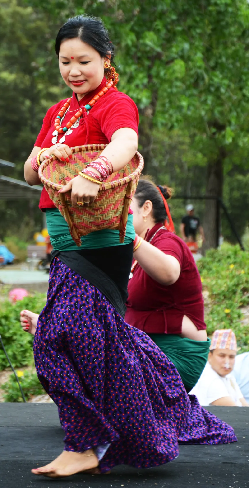 A woman in traditional dress with a bamboo basket dancing at a Maghe Sankranti celebration.